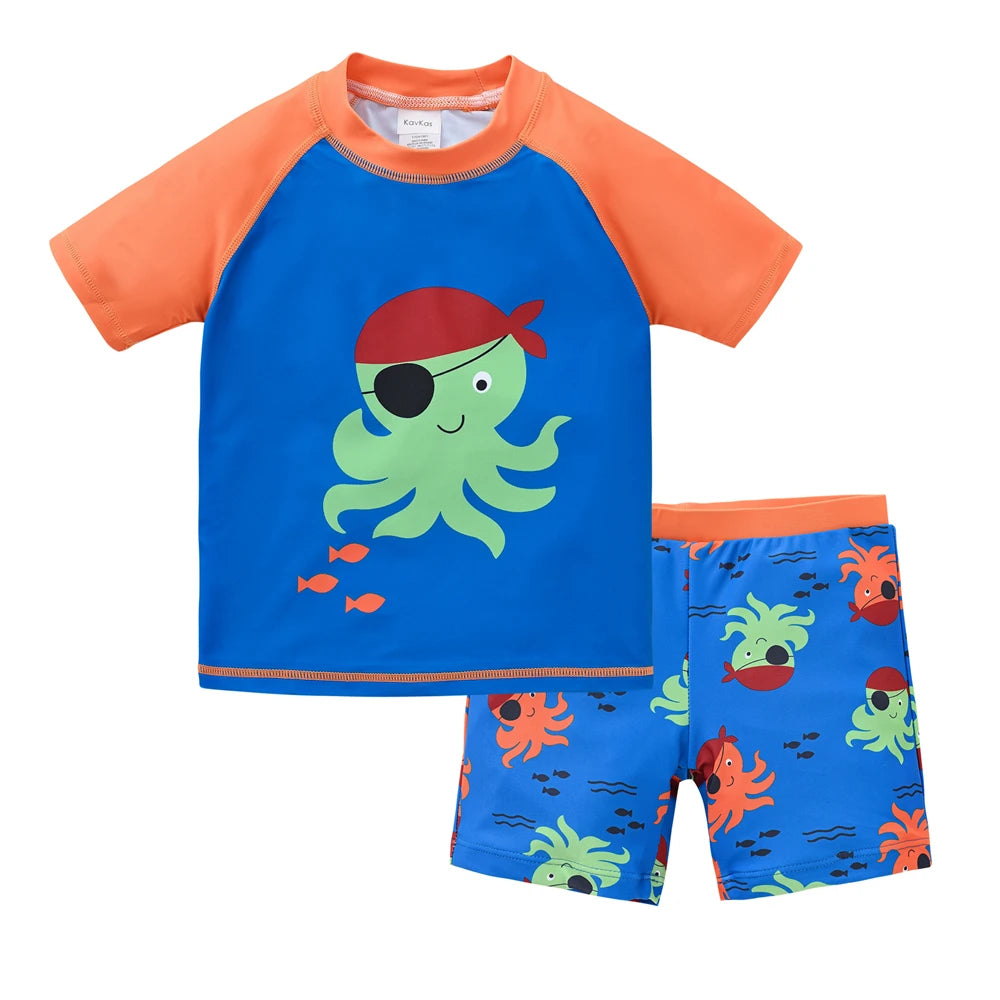 Boy wearing a blue and green two-piece swimsuit set with a cool print, for ages 1 to 7, by Baby Bubble, on a beach background.