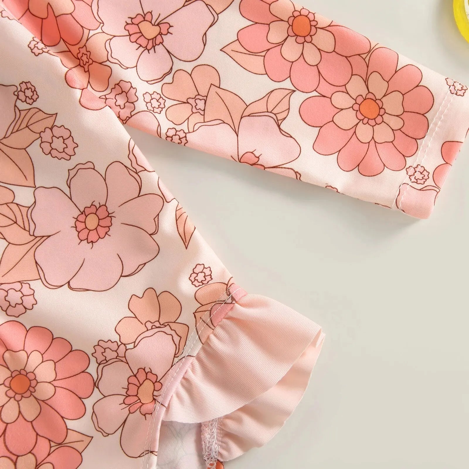 Baby girl in floral flamingo print one-piece swimsuit by Baby Bubble, showing the colorful swimsuit with ruffled straps.